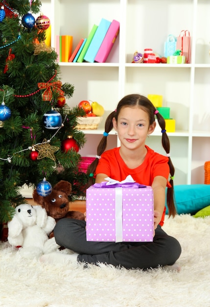 Klein meisje met geschenkdoos in de buurt van kerstboom