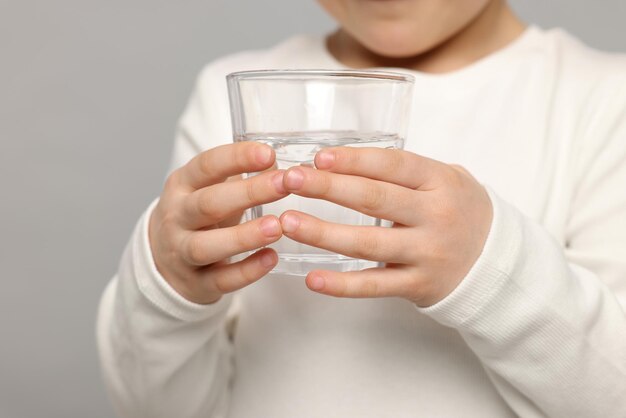 Klein meisje met glas zoet water op lichtgrijze close-up als achtergrond