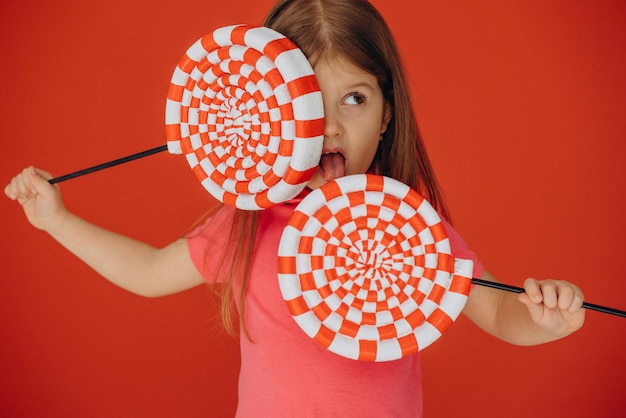 Klein meisje met grote lolly geïsoleerd op rode achtergrond