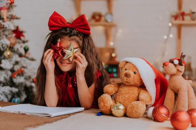 Klein meisje met haar favoriete beer in kerstmuts doet een kerstwens en schrijft een brief aan de kerstman