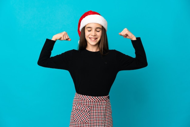 Klein meisje met kerstmuts geïsoleerd op blauwe achtergrond doen sterk gebaar