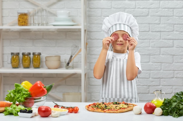 Klein meisje met koksmuts en een schort kokende pizza