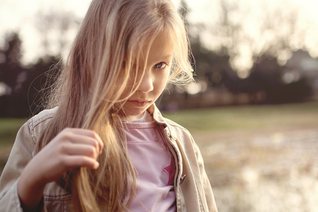 Klein meisje met lang haar, houdt een haarlok in haar hand en kijkt verlegen naar de camera.