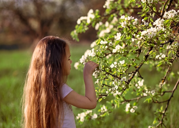 Klein meisje met lang haar in de buurt van een bloeiende boom