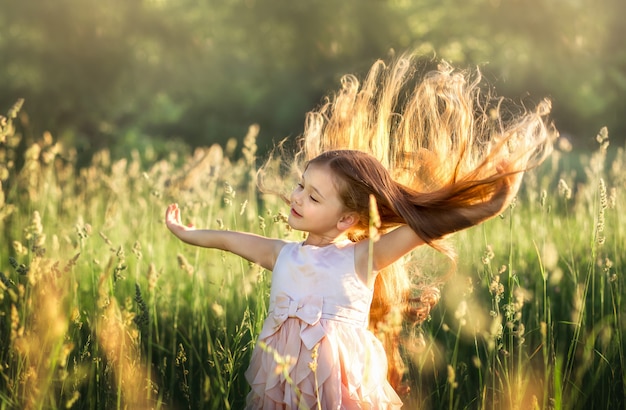 klein meisje met lang haar in een mooie jurk op de natuur in de zomer