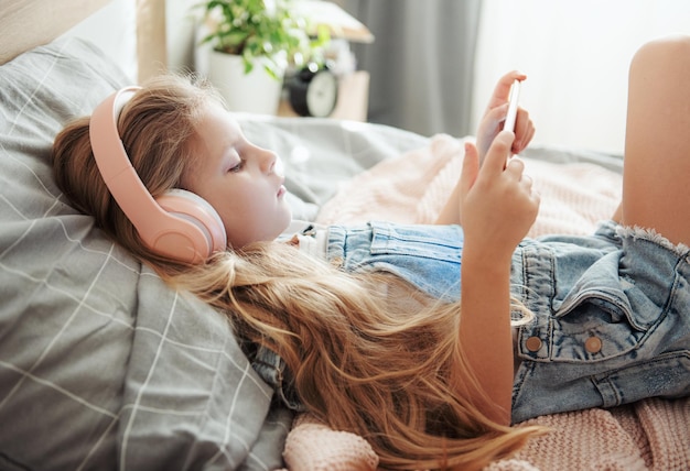 Klein meisje met mobiele telefoon die naar muziek luistert terwijl ze in bed ligt