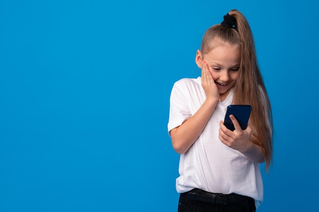 Klein meisje met mobiele telefoon tegen blauwe achtergrond