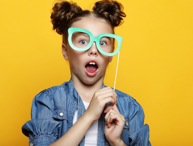 Klein meisje met papieren accessoires op gele achtergrond