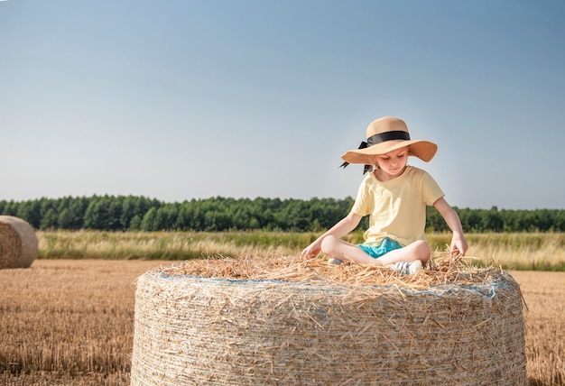 Klein meisje met plezier in een tarweveld op een zomerdag. Kind spelen op hooibaal veld tijdens de oogsttijd.