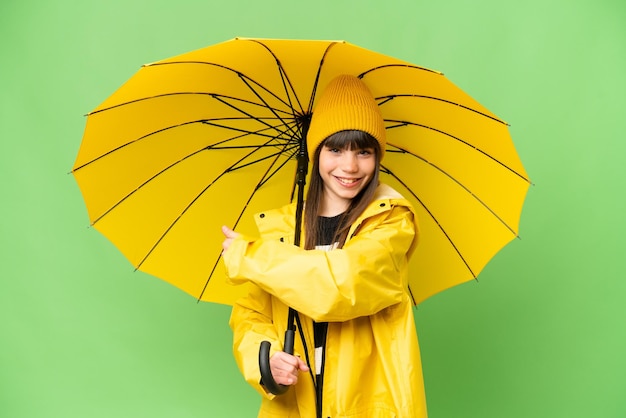 Klein meisje met regenbestendige jas en paraplu over geïsoleerde chroma key achtergrond die terug wijst