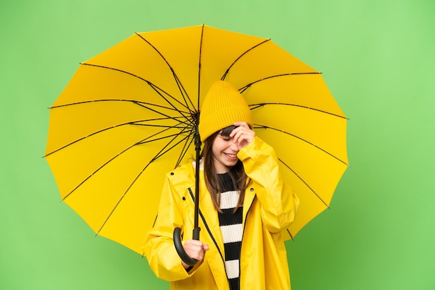 Klein meisje met regenbestendige jas en paraplu over geïsoleerde chroma key achtergrond lachen