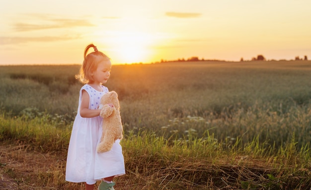 Klein meisje met teddybeer op weg bij zonsondergang