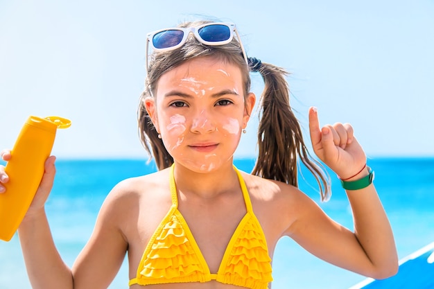 Klein meisje met zonnebrandcrème op haar gezicht op het strand