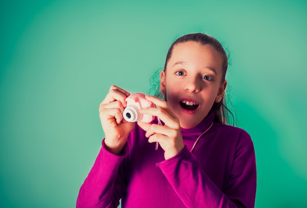 Klein meisje nemen foto met behulp van speelgoed fotocamera op cyaan achtergrond