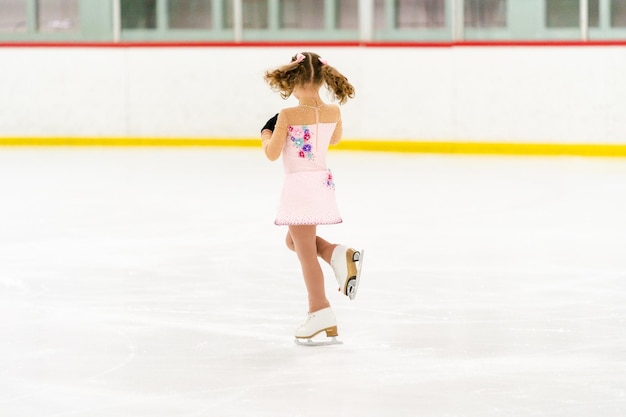 Klein meisje oefent kunstschaatsen op een overdekte ijsbaan