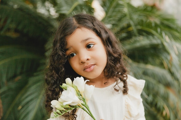 Klein meisje omringd door tropische bladeren Portret van een donker kind met donker haar Natuurlijke cosmetica gezondheid reinheid