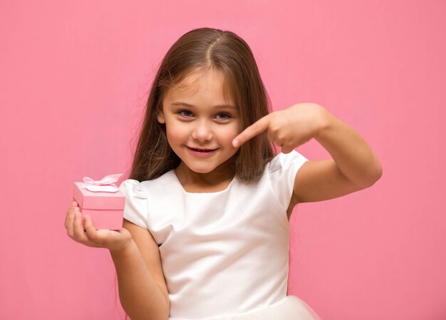 Klein meisje op een roze achtergrond toont een vinger op een geschenkdoos