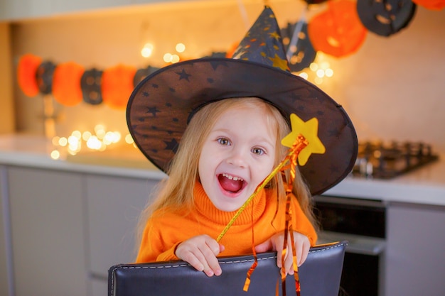 Klein meisje op Halloween in een heksenkostuum met een pompoen thuis in de keuken