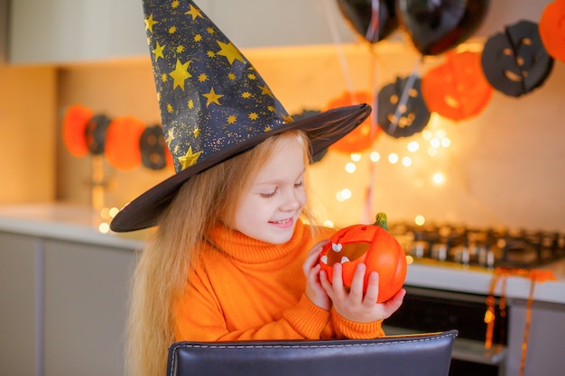 Klein meisje op Halloween in een heksenkostuum met een pompoen thuis in de keuken