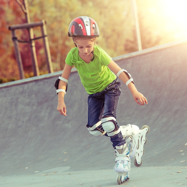 Klein meisje op rolschaatsen in helm in een park bij zonsondergang