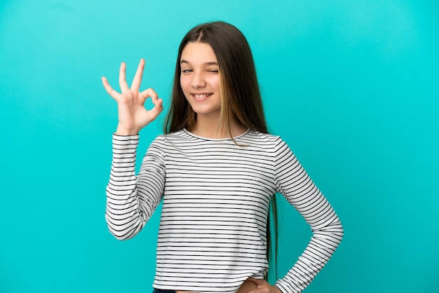 Klein meisje over geïsoleerde blauwe achtergrond die ok teken met vingers toont
