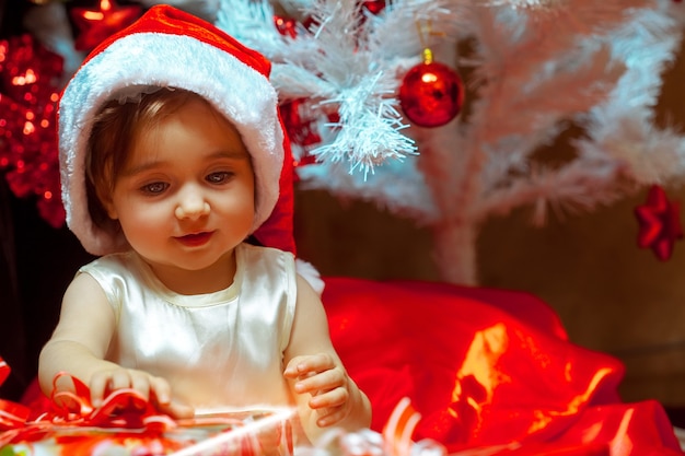 Klein meisje pakt het cadeau uit onder de kerstboom. Kerststemming. Nieuwjaar.