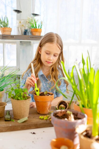 Klein meisje plant bloemen op het lente terras in het huis tuin zaailingen groeien landhuis veranda