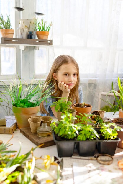 Klein meisje plant bloemen op het lente terras in het huis tuin zaailingen groeien landhuis veranda