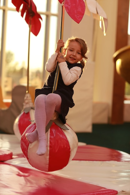 Klein meisje plezier in de speelkamer van de kinderen. Het meisje rijdt op een kindercarrousel in de vorm van een palmboom. Vrijetijds- en uitgaanscentrum.