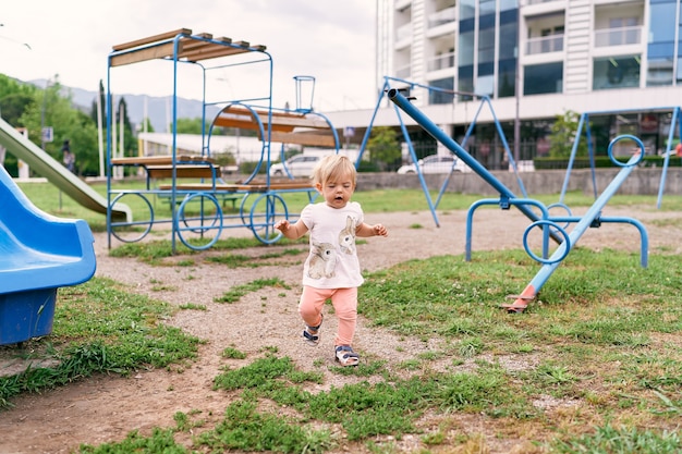 Klein meisje rent langs de speelplaats tegen de achtergrond van een flatgebouw