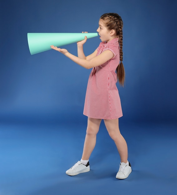 Klein meisje schreeuwen in papieren megafoon op kleur