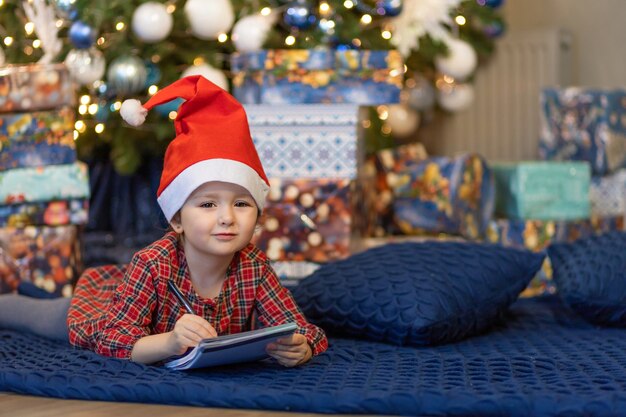 Foto klein meisje schrijft brief aan de kerstman. kinderdroom bij kerstboom over wens, cadeau op nieuwjaar