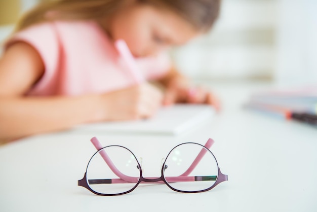 Foto klein meisje schrijft in schoolnotitieboekje wazig beeld bril voor visie in focus slecht zichtconcept