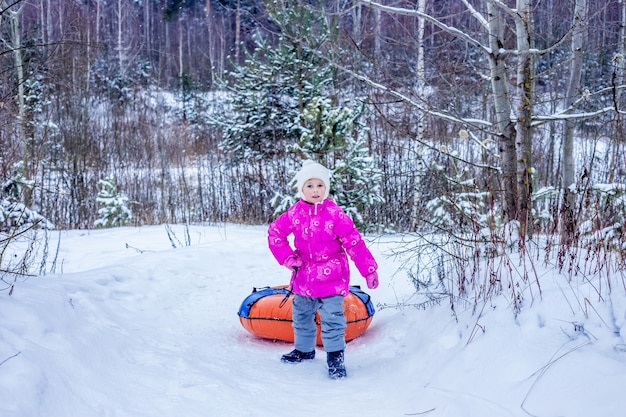 Klein meisje sleept glijbaan cheesecake op besneeuwde heuvel. Concept van winter buitenactiviteiten voor kinderen.