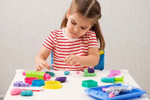 Klein meisje speelt enthousiast met plasticine-speeldeeg op witte tafel bij het creativiteitsconcept van kinderen thuis