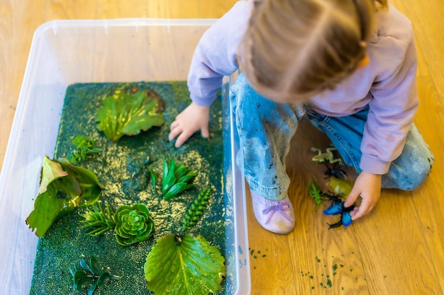 Klein meisje speelt in met de hand gemaakt moeras van groengekleurde chiazaden met insectenvissen en plantmodellen sens