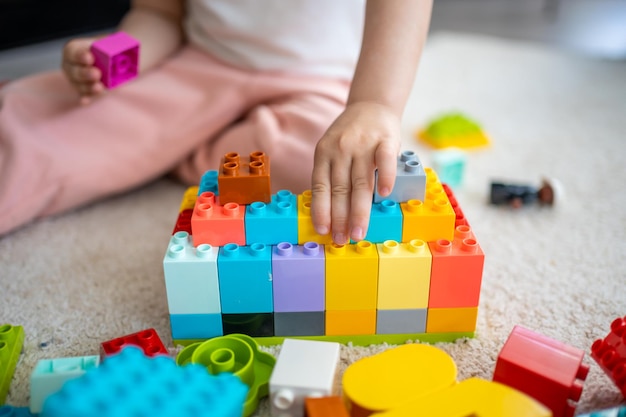 Klein meisje speelt met constructorspeelgoed op de vloer in een educatief spel voor thuisgebruik, tijdconcept voor vrijetijdsactiviteiten