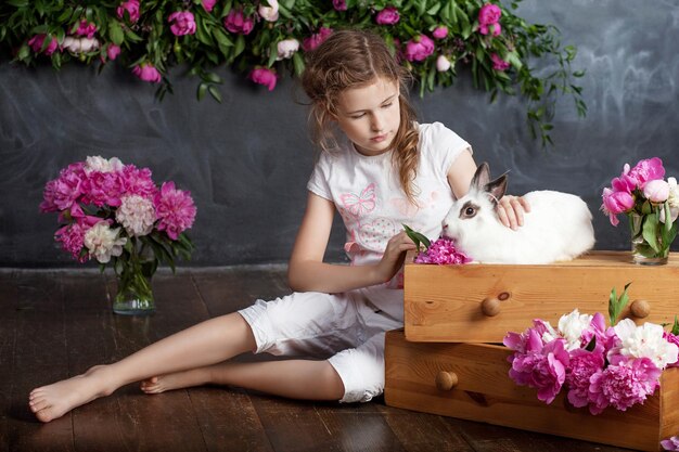 Klein meisje speelt met echt konijn Kind en wit konijntje op Pasen op bloemachtergrond Kinderen en huisdieren spelen Plezier en vriendschap voor dieren en kinderen