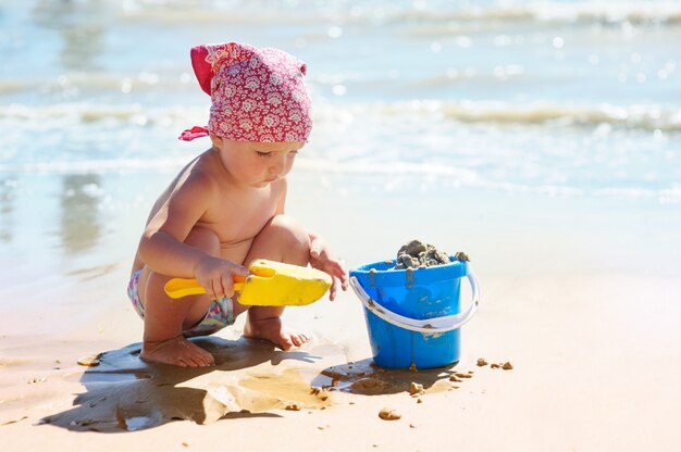 Klein meisje speelt met een blauwe emmer aan zee