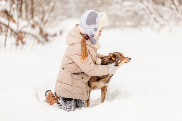 Klein meisje speelt met een hond in het winterbos. winter plezier