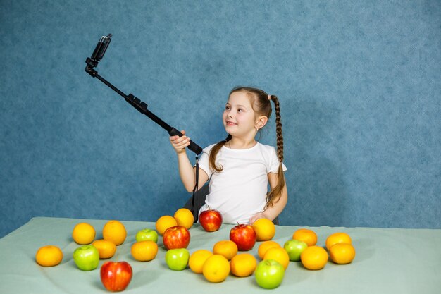 Klein meisje speelt met fruit en neemt een selfie aan de telefoon. Vitaminen en gezonde voeding voor kinderen.