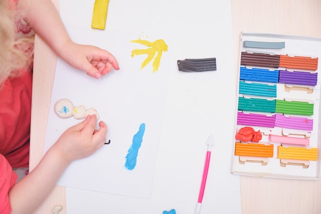 Klein meisje speelt met kleurrijke boetseerklei op tafel. home onderwijsspel met klei. vroeg ontwikkelingsconcept dat het kind beeldhouwt uit plasticine