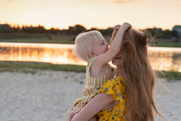 Foto klein meisje speelt met moeders haar. portret in beweging moeder en kind op rivier en zonsondergang.