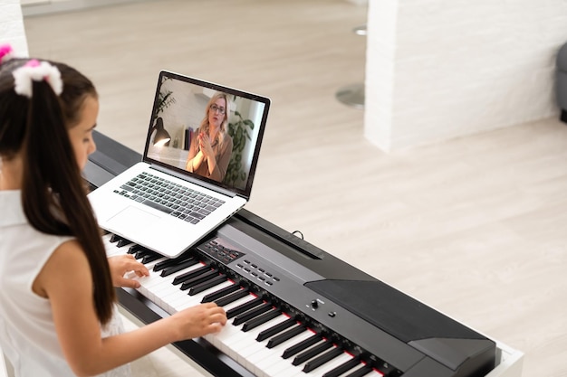 klein meisje speelt piano in klassikaal onderwijs met laptop thuis online leren in covid-19 crisisquarantaine.