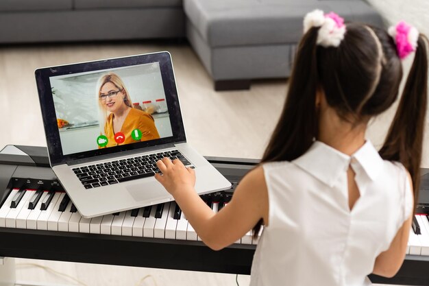 klein meisje speelt piano in klassikaal onderwijs met laptop thuis online leren in covid-19 crisisquarantaine.