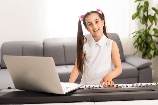 Klein meisje speelt piano in klassikaal onderwijs met laptop thuis online leren in covid-19 crisisquarantaine.