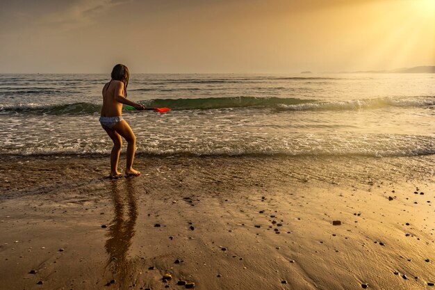 Klein meisje spelen met een schop in een zandstrand bij zonsondergang