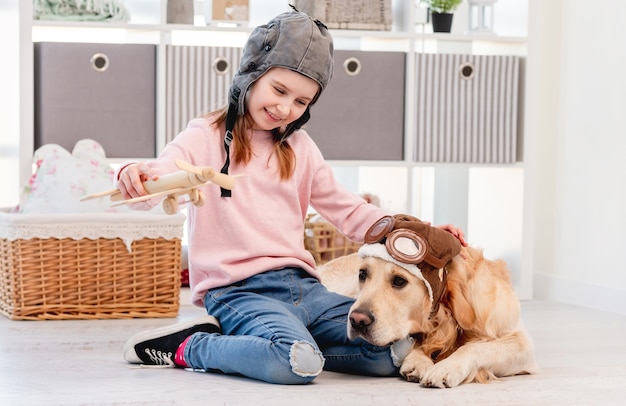 Klein meisje spelen met houten vlakte en golden retriever hond piloot bril liggend op de vloer