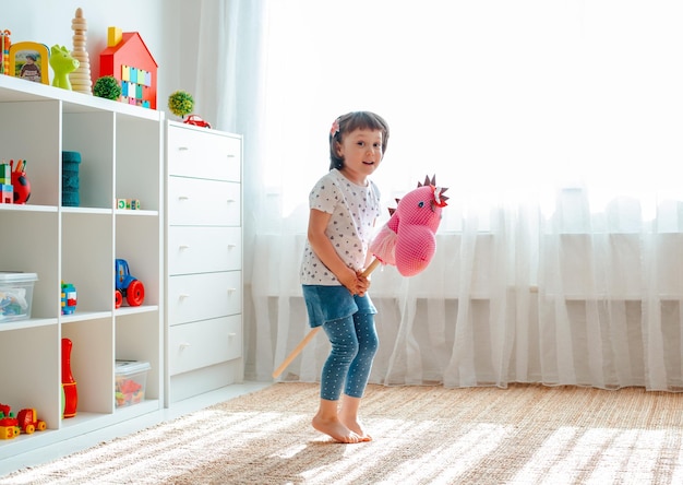 Klein meisje springt en rent op een paardenstok in de kinderkamer