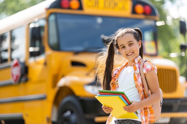 Klein meisje staat bij een grote schoolbusdeur met haar rugzak.